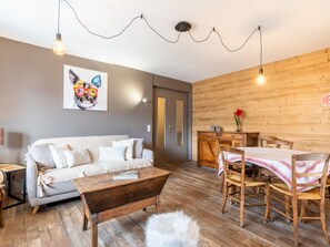 A cozy living room with a sofa, wooden dining table, and a painting on the wall. - 3* Apartment, 2 bedrooms, 6 guests, near slopes, WIFI (La Clusaz)