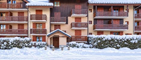 Un hotel de varios pisos con balcones, fachada de madera y alrededores cubiertos de nieve.