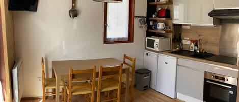 Une cuisine de taille réduite avec une table et des chaises en bois, un luminaire suspendu rouge, un four à micro-ondes, une machine à café et une cuisinière.