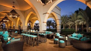 An outdoor lounge area with high arched ceilings, multiple seating arrangements, and a view of palm trees. - Jumeirah Zabeel Saray Royal Residence Lagoon Villa (Dubai)