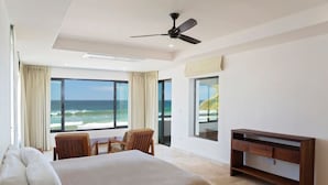 A hotel room with a bed, two chairs, a TV stand, and a large window offering a view of the ocean. - Iguana Beach House: Spacious Beachfront House with Swimming Pool (Hacienda Iguana)