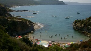 A coastal beach with rocky cliffs, clear blue water, and several boats.