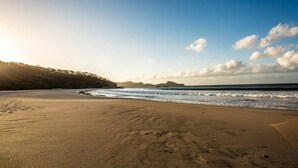 A beach with footprints leading to the water, a clear sky, and distant hills.