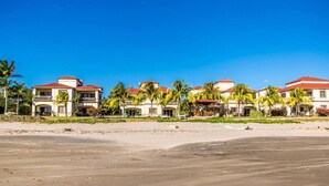 A beachfront hotel with multiple buildings, palm trees, and a sandy beach.
