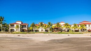 A beachfront hotel with multiple buildings, palm trees, and a sandy beach.