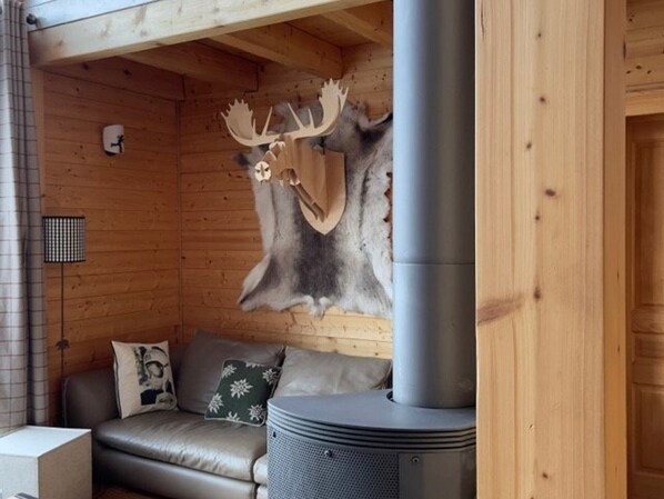 Interior acogedor de una cabaña con pared de madera, cabeza de alce montada, sofá y estufa de leña.