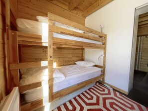 Una cama litera con estructura de madera, ropa de cama blanca y una alfombra estampada en el suelo.