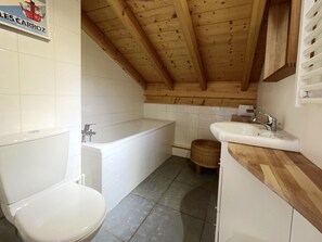 Un baño pequeño y funcional con techo de madera, una bañera, un inodoro y un lavamanos.