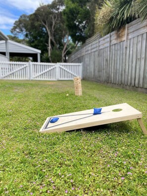 A lawn with a wooden board game set up, a white fence, and a wooden structure in the background. - Allure Beach House Rye. (Rye)