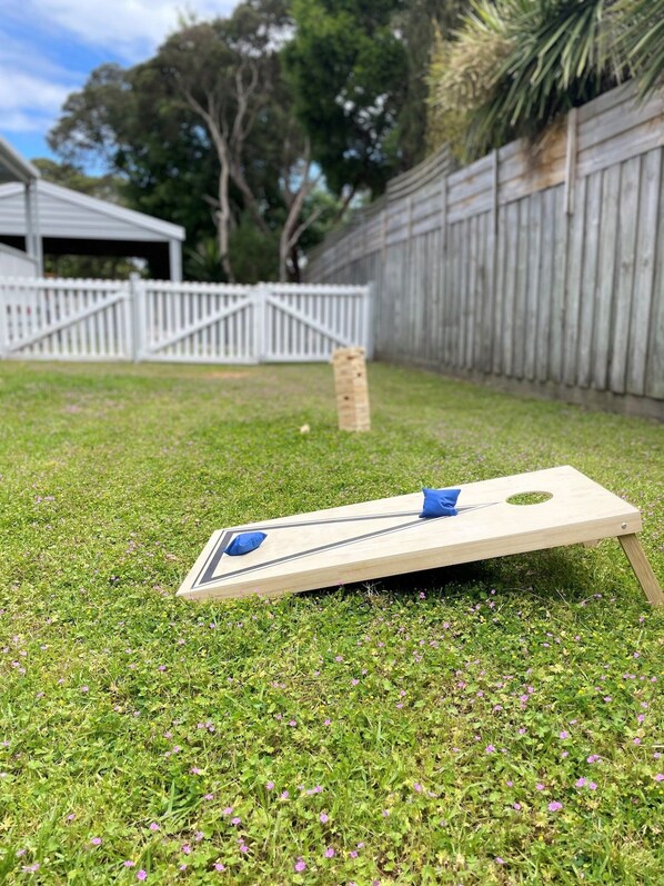 A lawn with a wooden board game set up, a white fence, and a wooden structure in the background. - Allure Beach House, Rye (Rye)