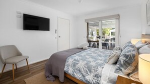 Una camera da letto con un letto, una sedia, una televisione e una porta finestra che dà su un'area esterna.