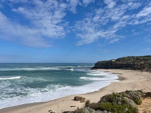 A beach with waves, a clear sky, and a rocky outcrop. - Allure Beach House Rye. (Rye)