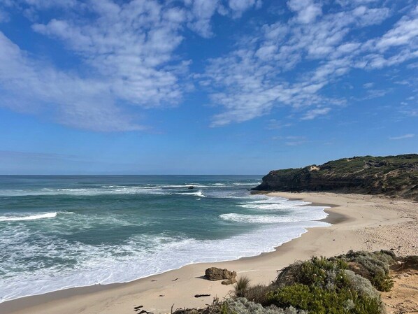Une plage avec des vagues, un ciel dégagé et un promontoire rocheux.