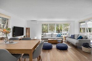 A modern living room with a wooden dining table, grey sofas, and a TV. - Allure Beach House, Rye (Rye)