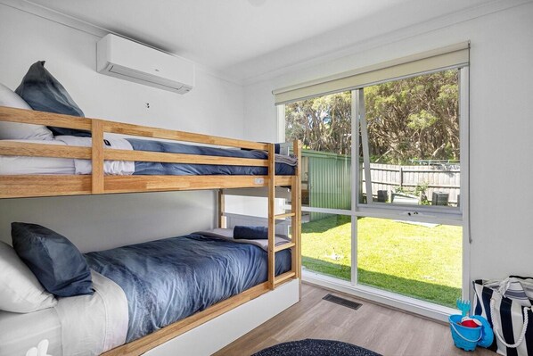 A bunk bed room with a large window, a small rug, and a bag on the floor. - Allure Beach House Rye. (Rye)