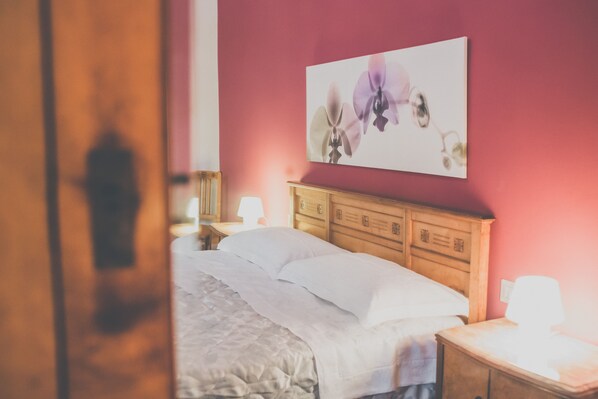 A bedroom with a wooden headboard, a bed with white linens, a nightstand with a lamp, and a wall-mounted floral artwork. - Palazzo Speciale B&B (Catania)
