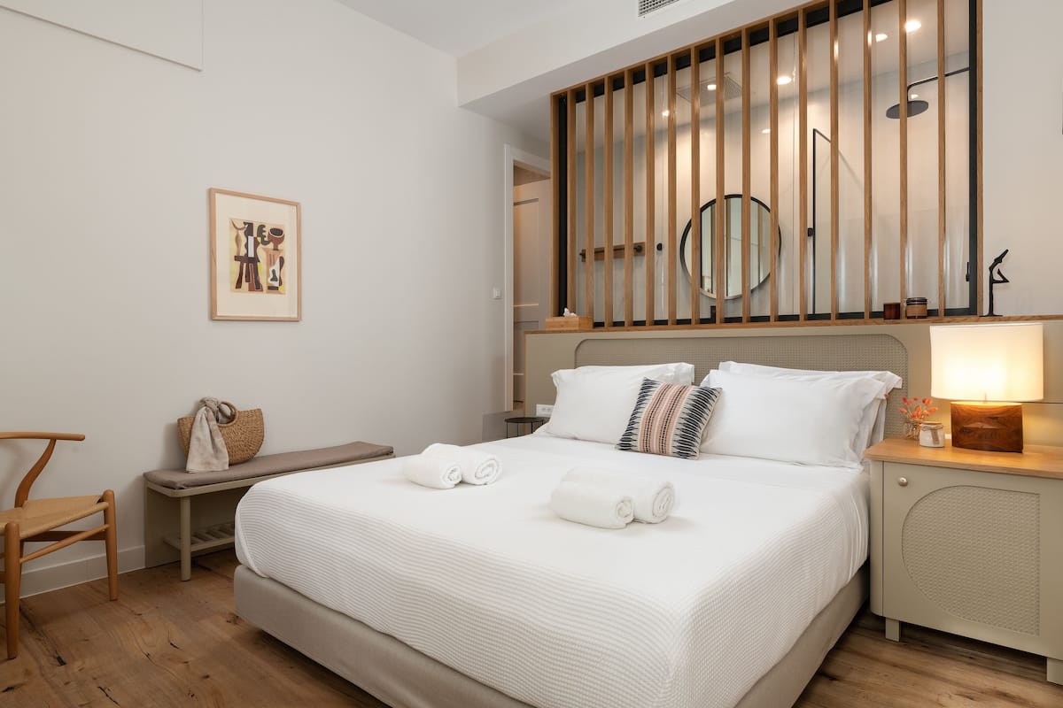 A neatly arranged hotel room with a bed, bedside table, and a small seating area.