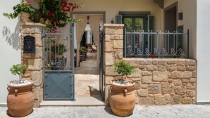 A stone wall entrance with a metal gate, potted plants, and a view into the interior. - Casa Natura (Rhodes)