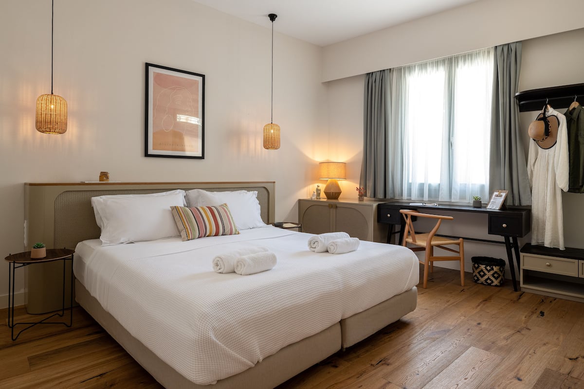 A hotel room with a large bed, bedside tables, a desk, a chair, and a wardrobe.