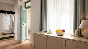 A room with a wooden floor, a white dresser with a bowl of fruit, a lamp, and a window with curtains. - Casa Natura (Rhodes)