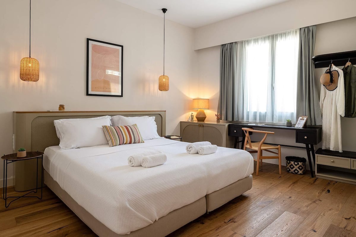 A hotel room with a bed, bedside tables, a desk, a chair, a lamp, a framed picture, and a wardrobe.