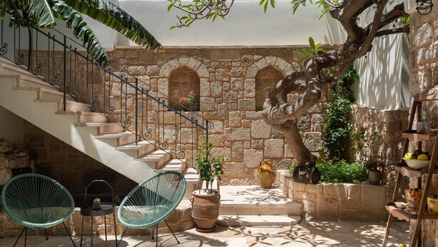 A stone staircase leading to an upper level, two green chairs, a potted plant, and a shelf with fruits and a vase. - Casa Natura (Rhodes)