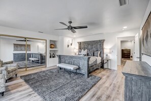 Ein Schlafzimmer mit einem Bett, Nachttischen, einem Spiegel und einem Deckenventilator.