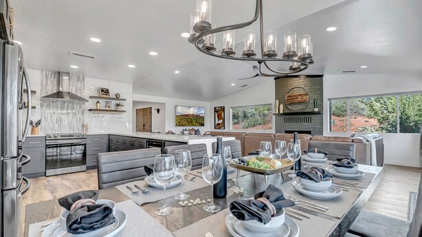 A modern kitchen with a central island, a dining area with a long table set for six, and a large window offering a view of the outdoors. - Prime Location, Walk To Restaurants, Enjoy The Sunrise And Red Rock Views (Sedona)