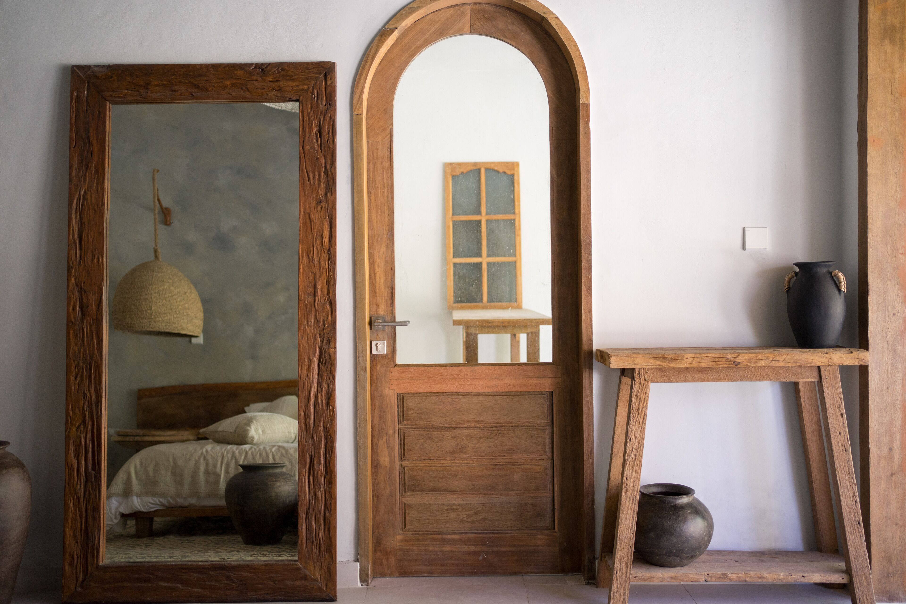 A rustic room with a wooden door, a mirror, a bed, and a small table with a vase.