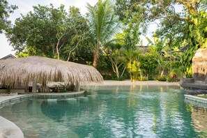 Une piscine dotée d’une structure de toit en chaume, entourée d’une végétation tropicale luxuriante.