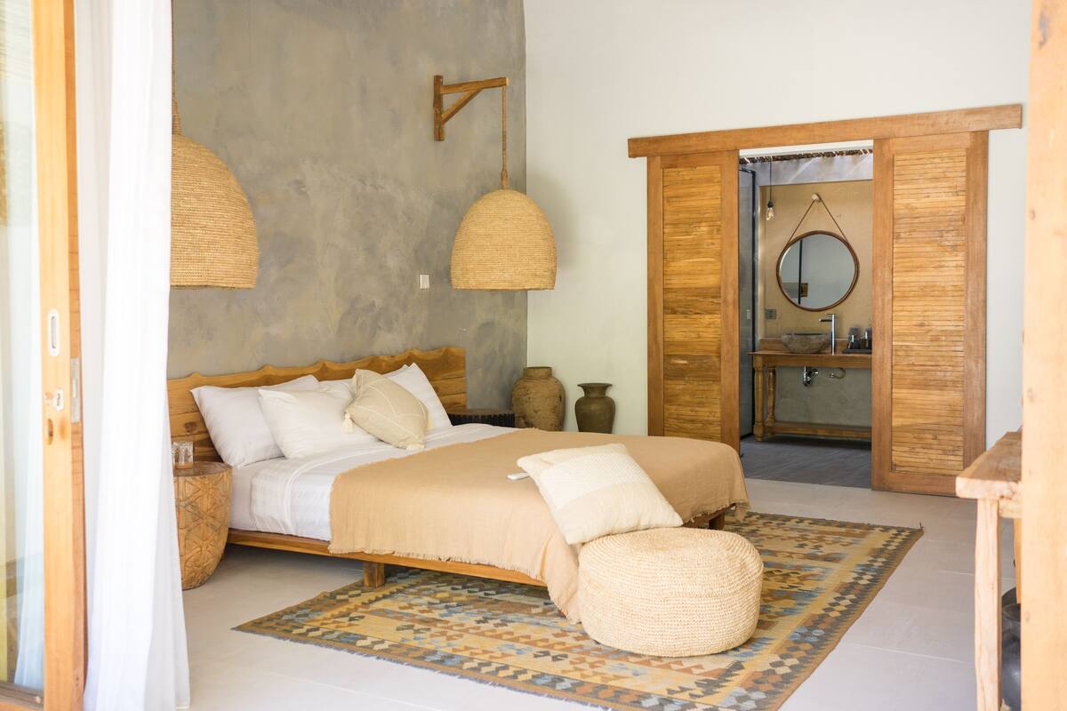 Un dormitorio con cama, un armario de madera, un baño con bañera y un espejo colgado.
