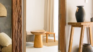 Una sala de estar moderna con suelo de madera, un ventilador de techo, un adorno circular tejido en la pared, una mesa de madera y un jarrón oscuro sobre un pedestal de madera.