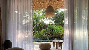 Una habitación con una cama, un pouf tejido, una mesa de madera y una lámpara colgante.