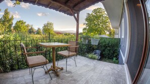 A covered patio with a table and chairs, a view of greenery and distant buildings, and a metal fence. - Yiğit Pansiyon (Sapanca)