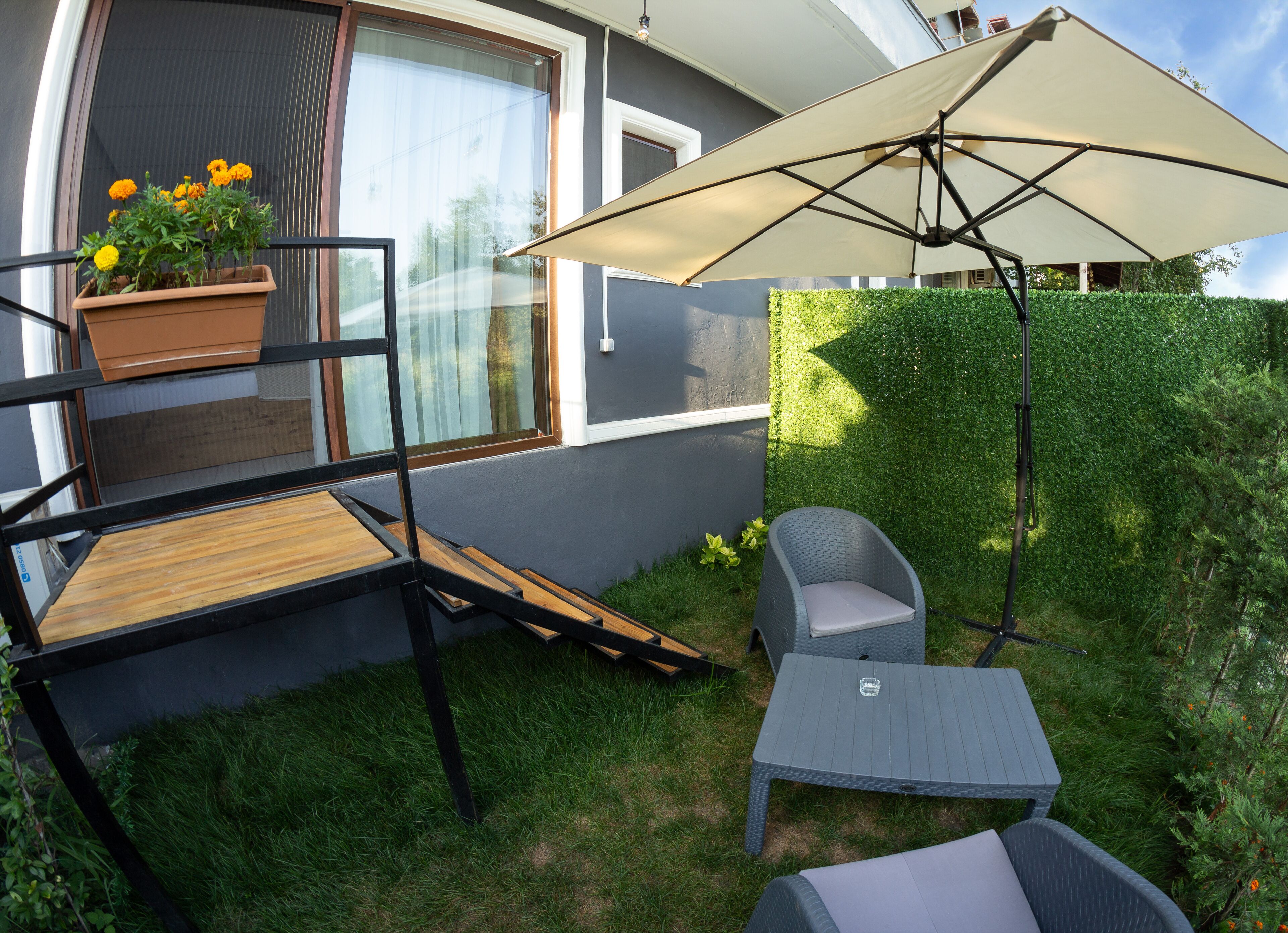 Un patio con una mesa de madera, una silla de mimbre gris y un paraguas grande.