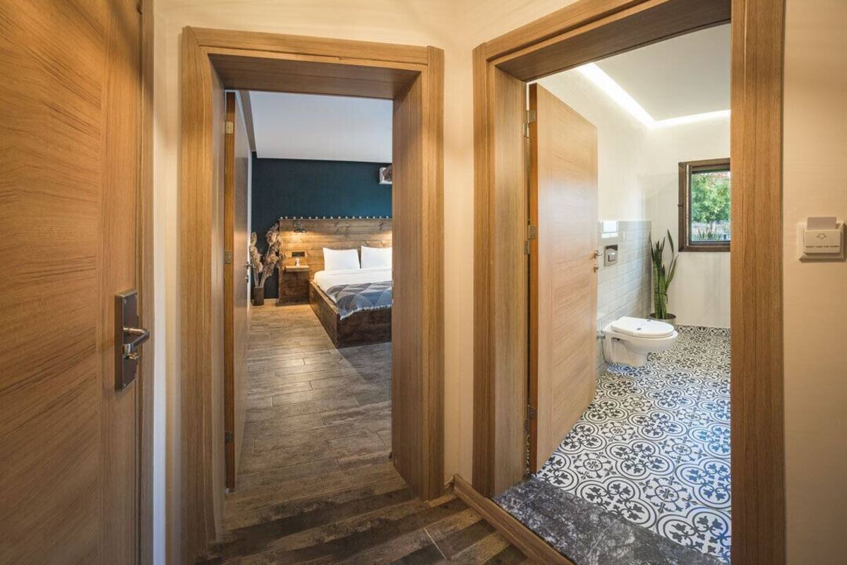 A hallway leading to a bedroom with a bed, a bathroom with a toilet, and a plant.