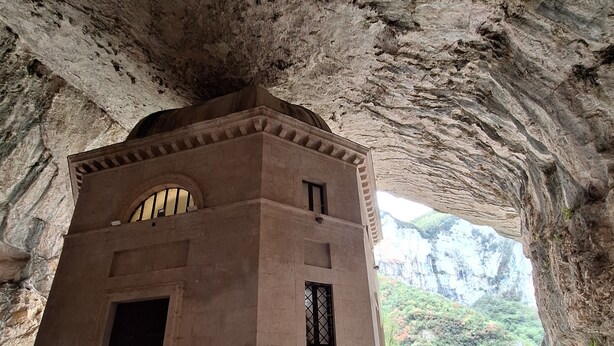 A stone building with arched windows and a door, located in a cave-like structure with natural rock formations visible in the background.