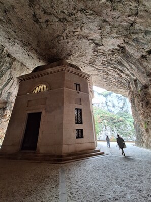 Un edificio de piedra con ventanas de arco y una puerta, situado en una estructura similar a una cueva, con formaciones rocosas naturales a la vista.