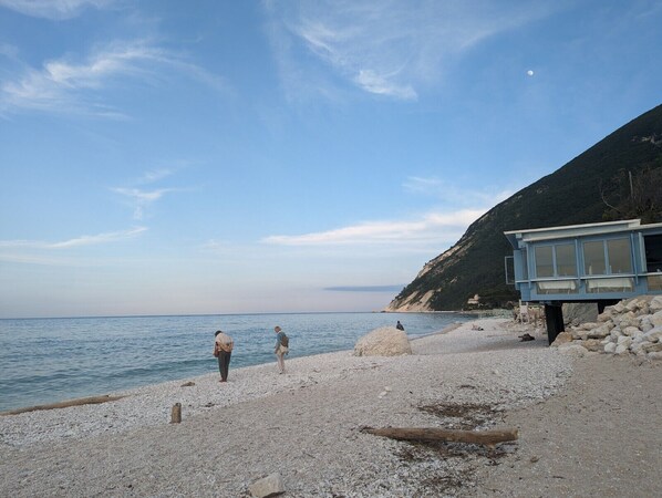 Una playa de guijarros con un pequeño edificio, cielo despejado y una montaña distante.