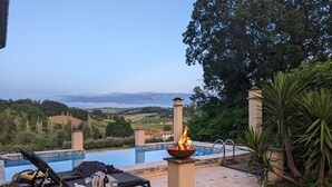 A poolside area with a fire feature, lounge chairs, and a view of the countryside.
