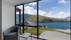 A room with a large window offering a view of a lake, mountains, and a road.