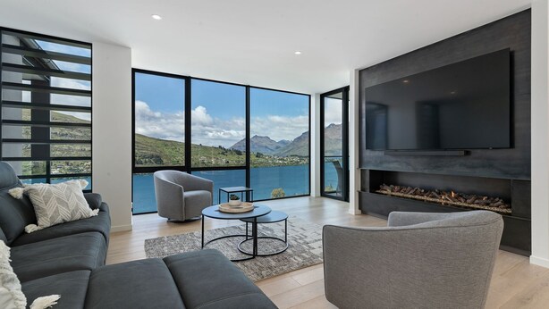 A modern living room with a large TV, comfortable seating, and a scenic lake view.