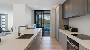 A modern kitchen with a large island, a built-in oven, and a view of a lake through a glass door.