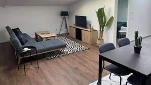 Ett modernt vardagsrum med en soffa, ett matbord, en tv och en växt.