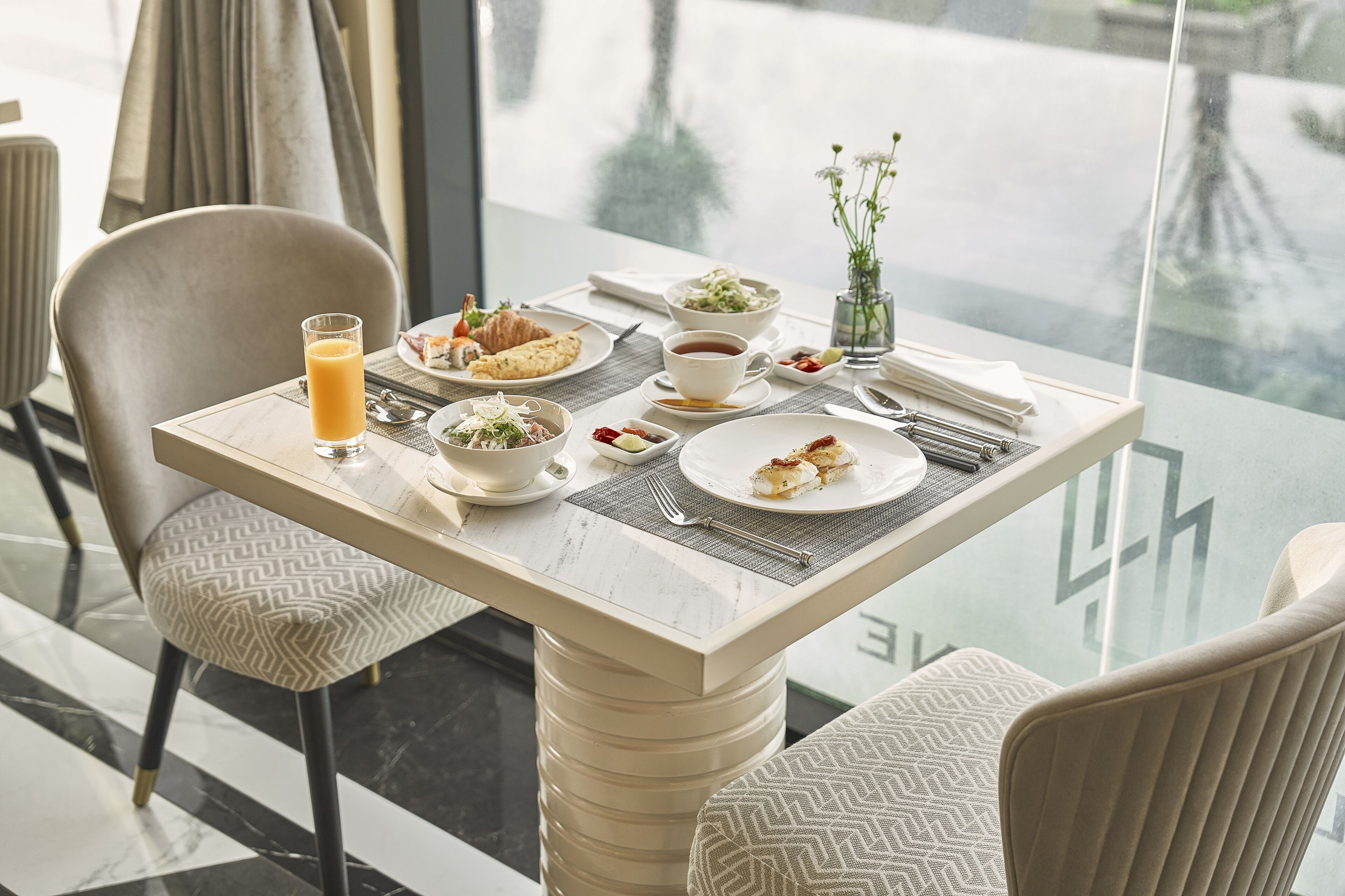 A dining table with plates of food, a glass of orange juice, and a cup of tea.