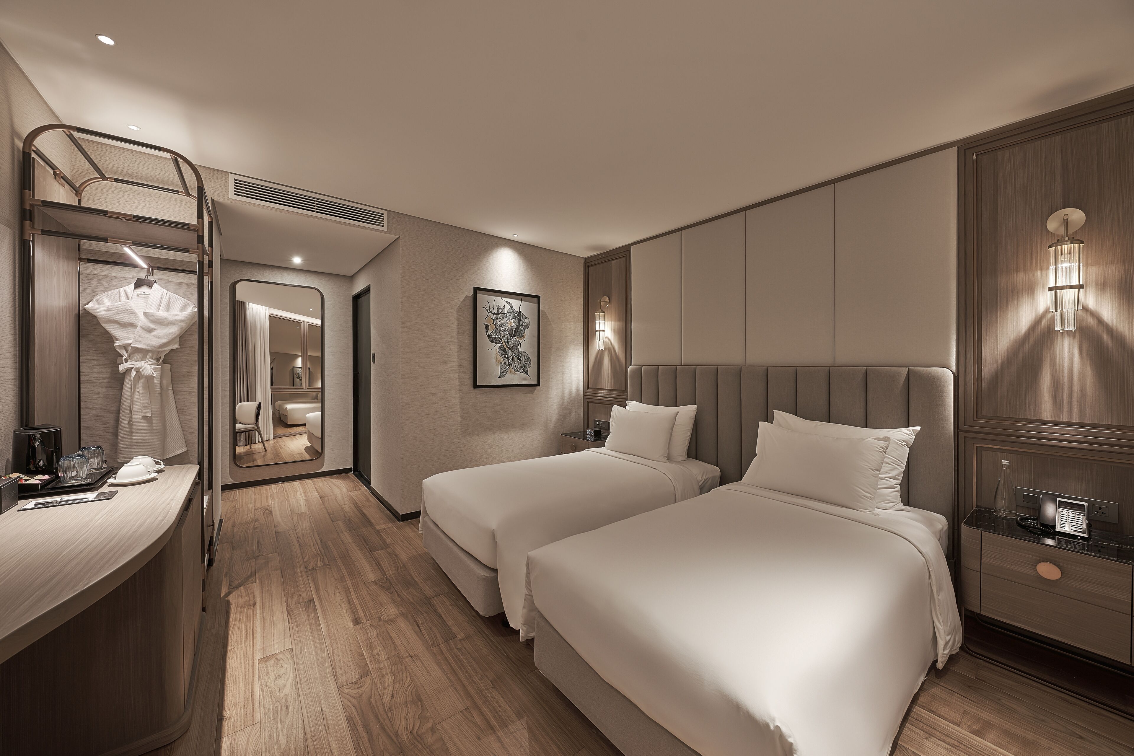 A hotel room with two beds, a desk, a mirror, and a nightstand with a lamp.