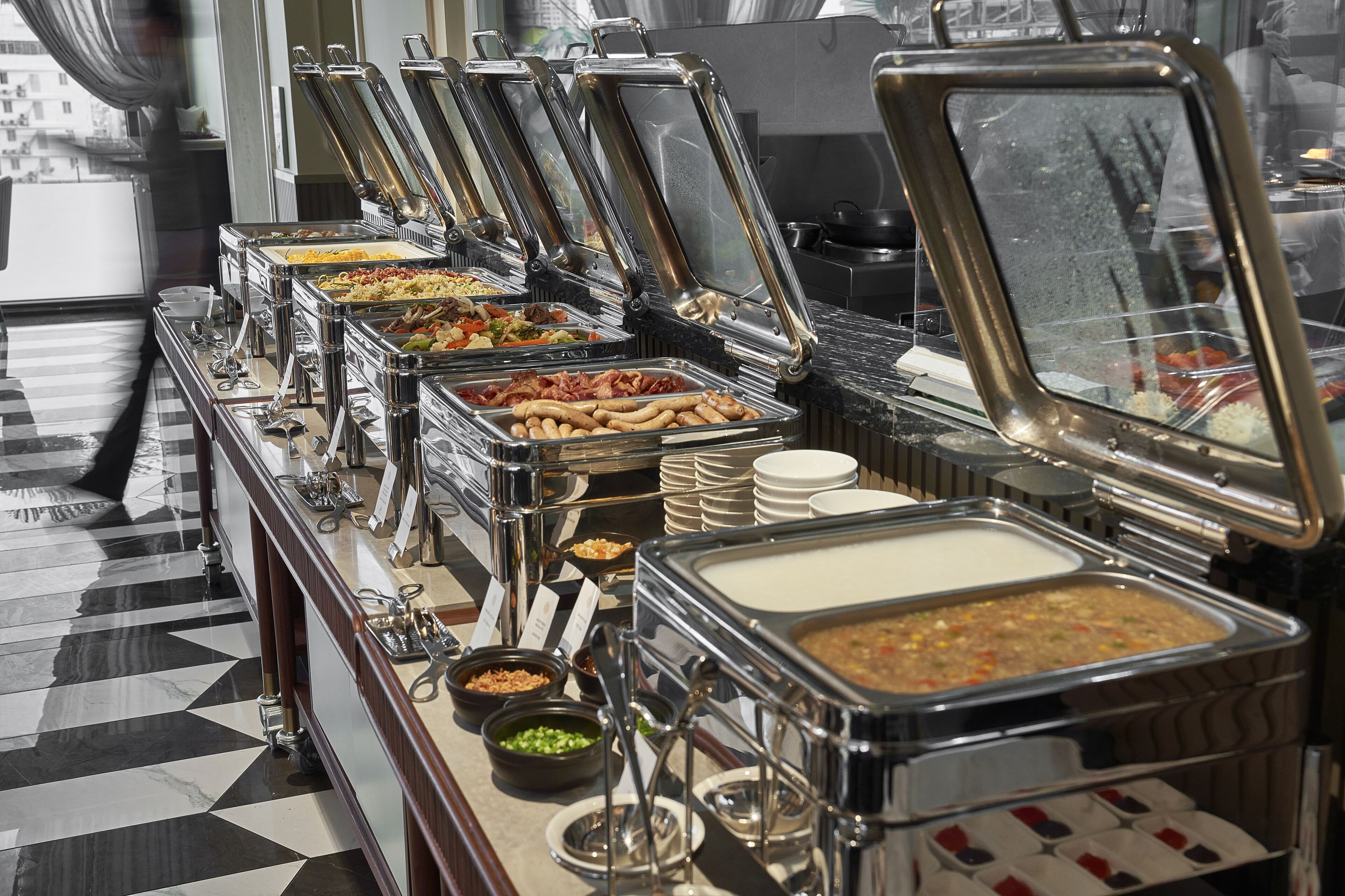 A buffet with various food options, including meats, vegetables, and soups, arranged on a marble floor.