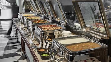 Ein reichhaltiges Buffet mit verschiedenen Speisen, darunter Fleisch, Gemüse und Suppen, auf einem Marmorboden.