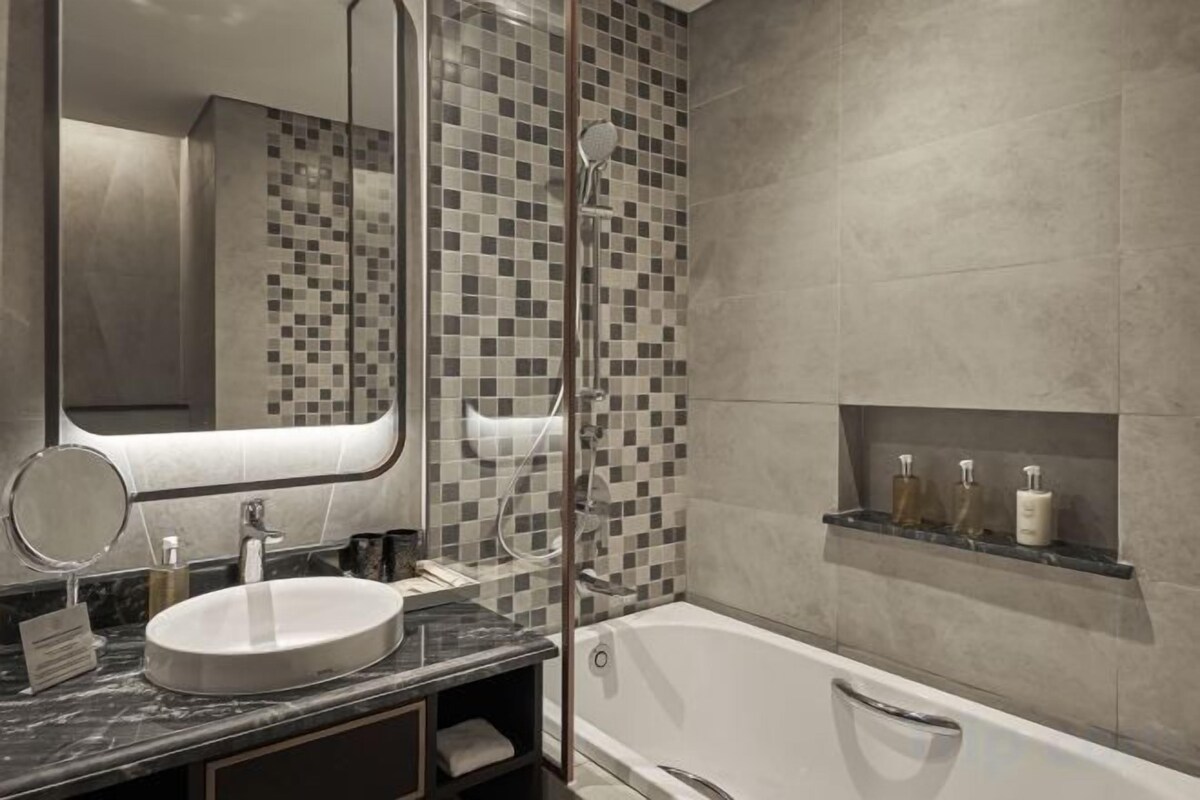 Un baño moderno con un lavabo redondo, un espejo grande, cabina de ducha con mampara de vidrio y una bañera.