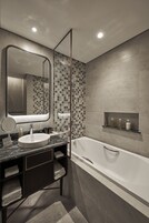 A modern bathroom with a large mirror, a sink, a shower, and a built-in shelf with toiletries.